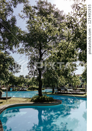 An elegant tropical resort with shady gardens and a winding pool surrounded by greenery. Turquoise water and a warm atmosphere of relaxation. An elite resort complex with crystal clear water. 125491935