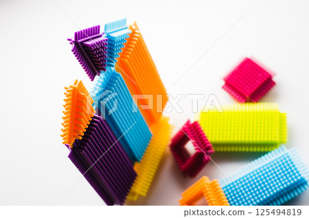 Bright parts of the construction toy form abstract objects. The children's building set appears lively and energetic against the light background. Bright parts of the construction toy form abstract objects. The children's building set appears lively and energetic against the light background. 125494819