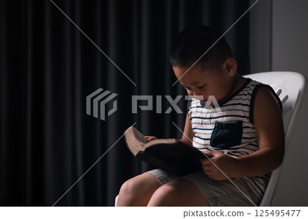 A little boy, full of faith, sits with the holy Bible in his hands, praying to God and embracing his Christian religion. child, person, bible, boy, religion, christian, holy, little, faith, god. 125495477