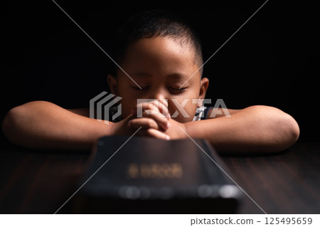 A little boy, full of faith, sits with the holy Bible in his hands, praying to God and embracing his Christian religion. child, person, bible, boy, religion, christian, holy, little, faith, god. 125495659