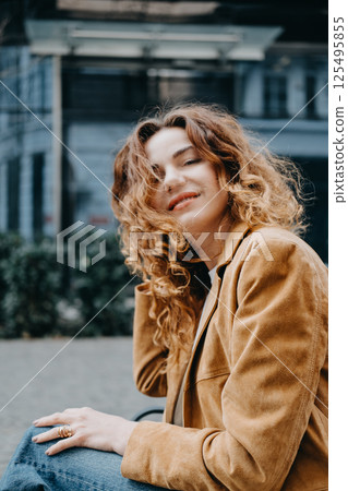 A young woman with curly red hair sits quietly on a bench looking down with a calm expression. Quiet contemplation, thoughtful mood, inner calm, soft elegance... 125495855