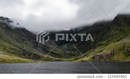 Majestic Coomloughra Lough nestled in rugged mountains of Ireland under dramatic clouds. Majestic Coomloughra Lough nestled in rugged mountains of Ireland under dramatic clouds. 125495902