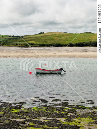 Tranquil Middle Ring Bay Beach in Ireland with a Small Boat Floating on Calm Waters. Tranquil Middle Ring Bay Beach in Ireland with a Small Boat Floating on Calm Waters. 125495903