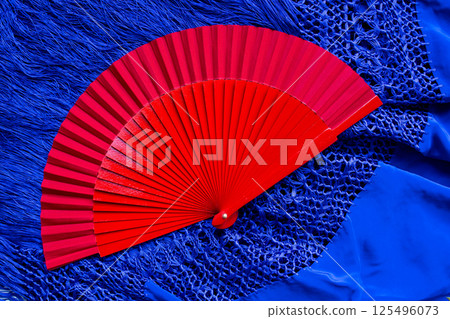 Vibrant red fan on blue lace fabric. A study in contrasts and textures 125496073