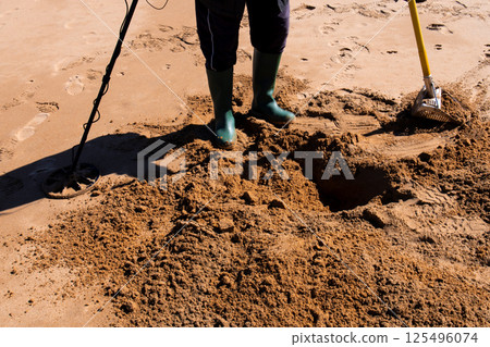 Person searching sandy beach with metal detector and shovel for treasures 125496074