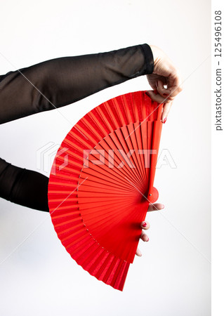 Female hand holding vibrant red fan against white background Female hand holding vibrant red fan against white background 125496108