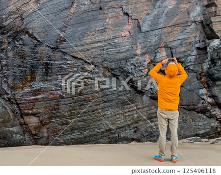 Caucasian male capturing rocky cliff texture in bright orange jacket Caucasian male capturing rocky cliff texture in bright orange jacket 125496118