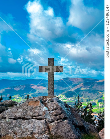 Stone cross on rocky cliff overlooking verdant landscape and dramatic sky Stone cross on rocky cliff overlooking verdant landscape and dramatic sky 125496147