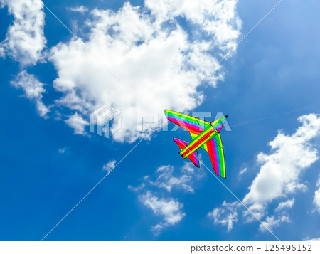 Colorful rainbow kite flying in a clear blue sky with fluffy clouds Colorful rainbow kite flying in a clear blue sky with fluffy clouds 125496152