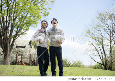 Image of a worker in work clothes, such as construction management, with fresh greenery in the background, whole body looking up at the future with arms around shoulders Image of a worker in work clothes, such as construction management, with fresh greenery in the background, whole body looking up at the future with arms around shoulders 125496942