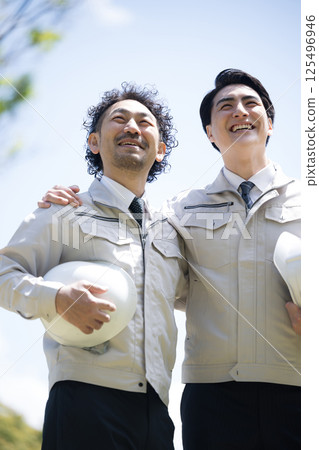 工人們穿著工作服站在建築管理等建築物前，背景是新鮮的綠色植物，他們互相摟著肩膀，抬頭看著未來 125496946