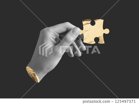 Hand holding one golden jigsaw puzzle piece. Human finger with textured foil element, black 125497371
