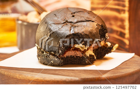 Black Hamburger close-up. A bitten hamburger lies on the table. Fast food. Black Hamburger close-up. A bitten hamburger lies on the table. Fast food. 125497702