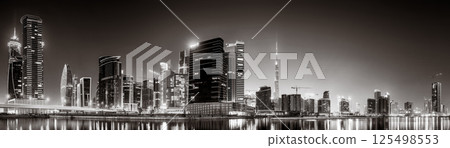 Urban city skyline with illuminated skyscrapers and waterfront railing in black and white at night, Dubai Marina bay UAE 125498553
