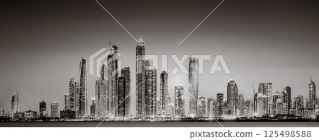 Urban city skyline with illuminated skyscrapers and waterfront railing in black and white at night, Dubai Marina bay UAE Urban city skyline with illuminated skyscrapers and waterfront railing in black and white at night, Dubai Marina bay UAE 125498588