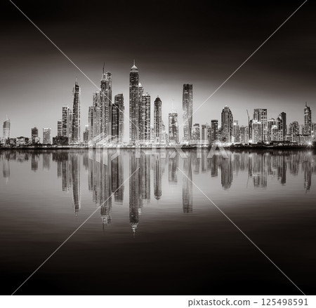 Urban city skyline with illuminated skyscrapers and waterfront railing in black and white at night, Dubai Marina bay UAE Urban city skyline with illuminated skyscrapers and waterfront railing in black and white at night, Dubai Marina bay UAE 125498591