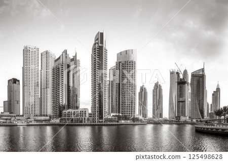 Monochrome city skyline with tall skyscrapers reflecting on calm water under a cloudy sky, Dubai Marina bay UAE Monochrome city skyline with tall skyscrapers reflecting on calm water under a cloudy sky, Dubai Marina bay UAE 125498628