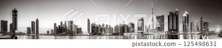 Monochrome city skyline with tall skyscrapers reflecting on calm water under a cloudy sky, Dubai Marina bay UAE Monochrome city skyline with tall skyscrapers reflecting on calm water under a cloudy sky, Dubai Marina bay UAE 125498631