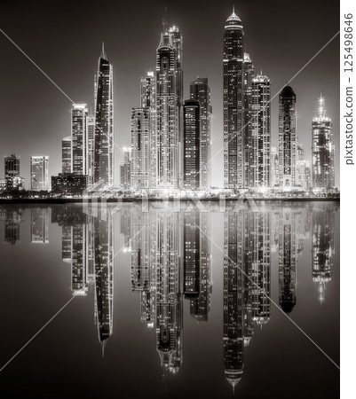 Urban city skyline with illuminated skyscrapers and waterfront railing in black and white at night, Dubai Marina bay UAE 125498646