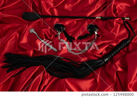 Adult sex games. Kinky lifestyle. Spank and whip ridding crop on the red linen. Bdsm outfit 125498800