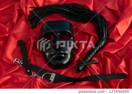 Adult sex games. Kinky lifestyle. Mask and whip ridding crop on the red linen. Bdsm outfit Adult sex games. Kinky lifestyle. Mask and whip ridding crop on the red linen. Bdsm outfit 125498804