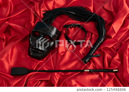 Adult sex games. Kinky lifestyle. Mask and whip ridding crop on the red linen. Bdsm outfit Adult sex games. Kinky lifestyle. Mask and whip ridding crop on the red linen. Bdsm outfit 125498806