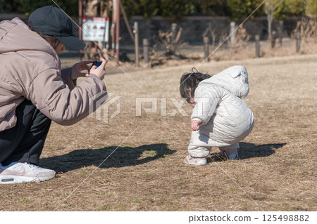 [A one-year-old child and his mother playing on the grass at Sagamihara Municipal Asamizo Park, using a smartphone] 125498882