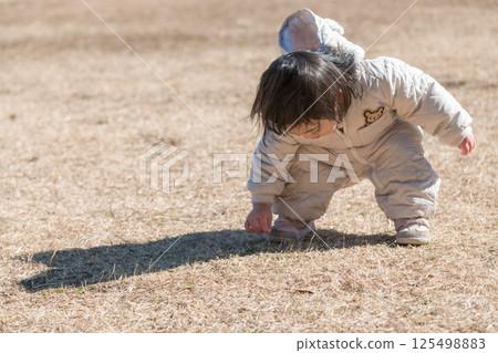 [One-year-old child crouching down while playing on the grass at Sagamihara Municipal Asamizo Park] 125498883