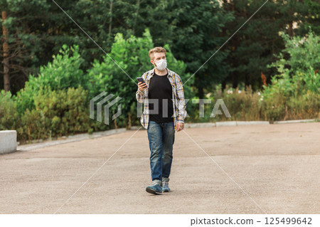 Man wearing a mask while walking in the park and checking his smartphone. Concept of modern life, health safety, and communication during pandemic times. Copy space Man wearing a mask while walking in the park and checking his smartphone. Concept of modern life, health safety, and communication during pandemic times. Copy space 125499642