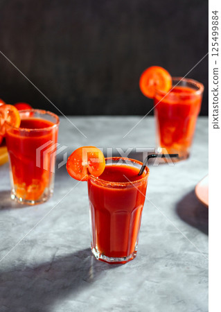 Three vegetable shaken cocktail in glass on dark grey background. Red tomato cocktail. Served with tomato slice. Vegan menu. 125499884