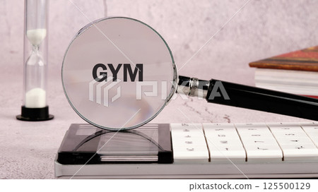 A concept word GYM through a magnifying glass surrounded by a calculator, hourglass and books, emphasizing the focus of the business and strategy 125500129
