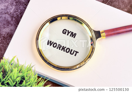The concept of a healthy lifestyle. The words GYM WORKOUT through a magnifying glass, top view on a blank sheet of notepad 125500130
