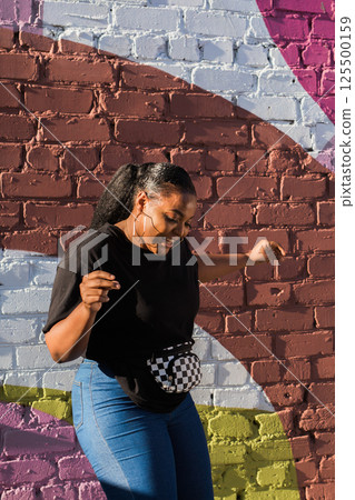 African american woman dancing near colorful brick wall during sunny day. Concept of joy, freedom, youth culture and positive urban lifestyle. African american woman dancing near colorful brick wall during sunny day. Concept of joy, freedom, youth culture and positive urban lifestyle. 125500159