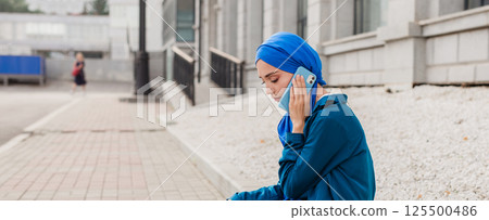 Young muslim woman in hijab speaking on the phone in urban surroundings. Communication, technology, and cultural diversity concepts. Banner with copy space 125500486