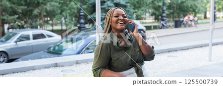 Smiling african american woman with braids talking on smartphone outdoors. Concept of joy, friendship and positive communication. Banner with copy space 125500739