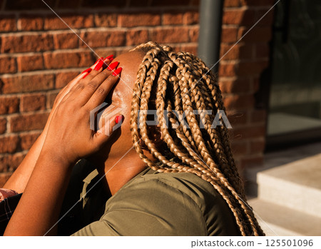 African american woman covering her face with her hands in bright sunlight outdoors. Emotion, fatigue, and real human moments of vulnerability. African american woman covering her face with her hands in bright sunlight outdoors. Emotion, fatigue, and real human moments of vulnerability. 125501096
