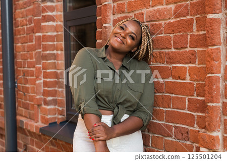 African american woman laughing joyfully while standing on a city street on a sunny day. Freedom, positivity, and happiness in an urban environment 125501204