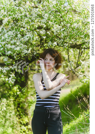 Woman touching face under blooming spring tree outdoors. Woman touching face under blooming spring tree outdoors. 125501668