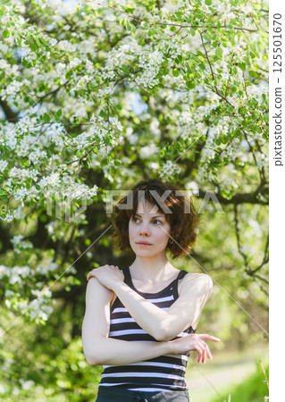 Woman looking aside under blooming tree in spring garden. Woman looking aside under blooming tree in spring garden. 125501670
