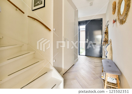 A stylish hallway featuring a staircase, minimalistic decor, and abundant natural light streaming through the door, creating an inviting atmosphere. 125502351