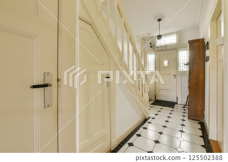 A well-lit modern hallway featuring a staircase, decorative elements, and a stylish entrance door. The design emphasizes clean lines and elegant decor. 125502388