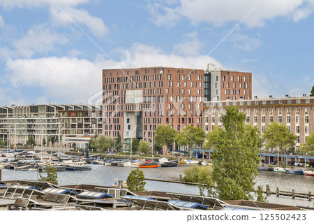 Showcasing contemporary buildings alongside a marina, this image features a blend of urban design and nature with boats docked and greenery thriving. Showcasing contemporary buildings alongside a marina, this image features a blend of urban design and nature with boats docked and greenery thriving. 125502423