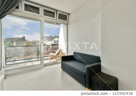 This contemporary living room features a sleek design with a comfortable sofa and large windows offering a picturesque balcony view, perfect for relaxation. 125502438