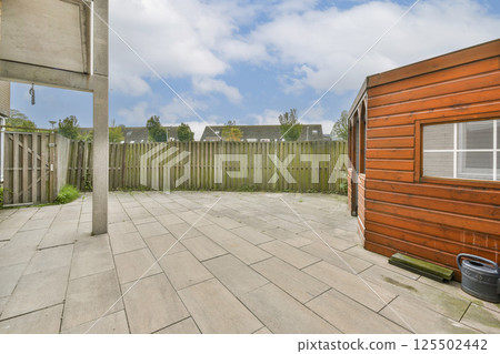 A tranquil outdoor area featuring a wooden structure, paved flooring, and a backdrop of greenery under a blue sky. Perfect for relaxation or gatherings. A tranquil outdoor area featuring a wooden structure, paved flooring, and a backdrop of greenery under a blue sky. Perfect for relaxation or gatherings. 125502442