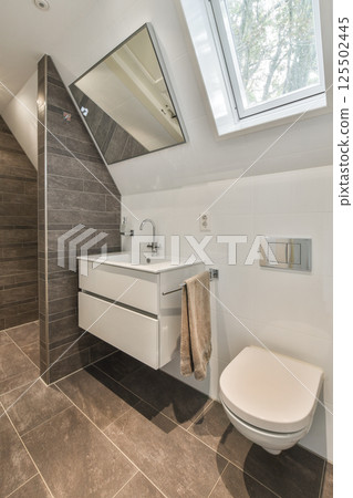 A contemporary bathroom featuring sleek cabinetry, stylish fixtures, and a minimalistic aesthetic. Natural light flows in through the skylight, enhancing the space. 125502445