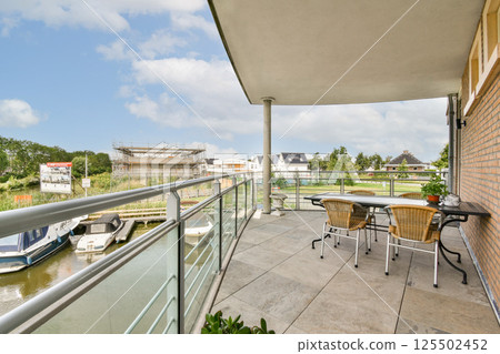 A stylish balcony overlooking a serene waterway, featuring contemporary furniture and lush greenery, perfect for relaxation and leisure. 125502452