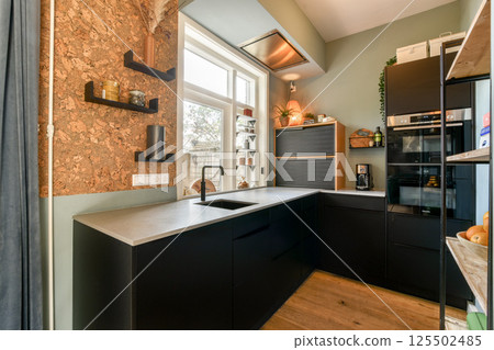 A stylish kitchen featuring sleek black cabinetry, a metallic countertop, and natural light enhancing its contemporary aesthetic. A stylish kitchen featuring sleek black cabinetry, a metallic countertop, and natural light enhancing its contemporary aesthetic. 125502485