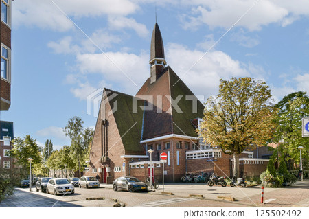 A picturesque historic church stands elegantly amidst a lively urban backdrop, featuring beautiful trees and a vibrant sky. Ideal for architecture enthusiasts. 125502492
