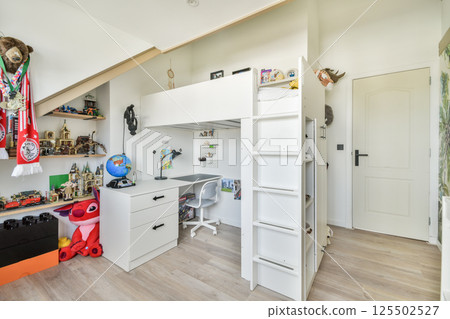 This inviting children's room features a loft bed, colorful decor, and a fun play area. Shelves display toys and trophies adding to the lively atmosphere. 125502527