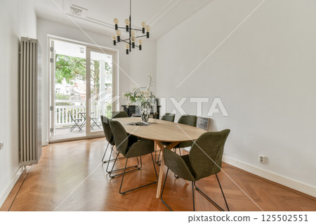 A stylish dining room featuring a wooden table surrounded by contemporary chairs, highlighted by ample natural light from the large windows. 125502551